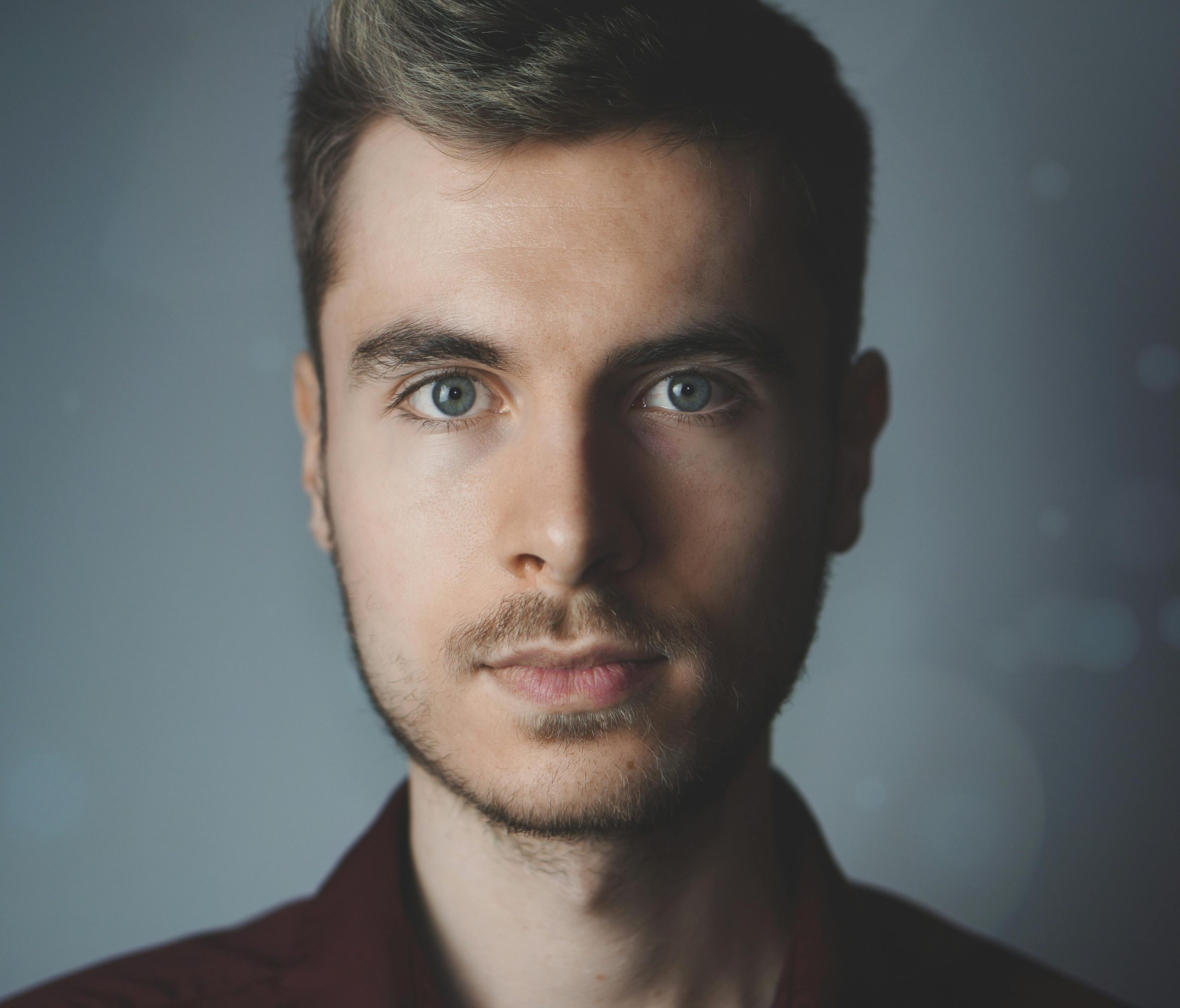 Close-up portrait of a young man with facial hair and a serious expression.